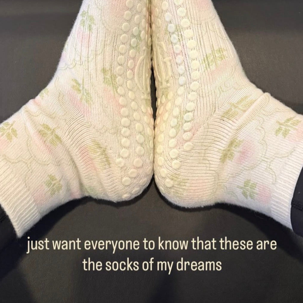 White socks with floral patterns worn indoors on a dark pilates reformer grip sock