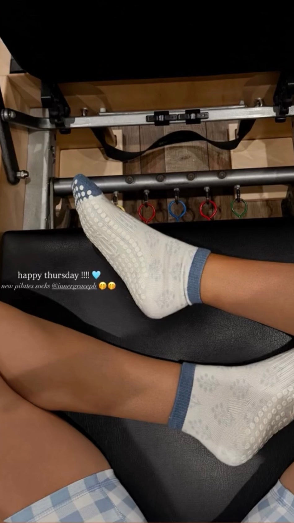 Person wearing white pilates grip socks with blue accents on a gym machine.