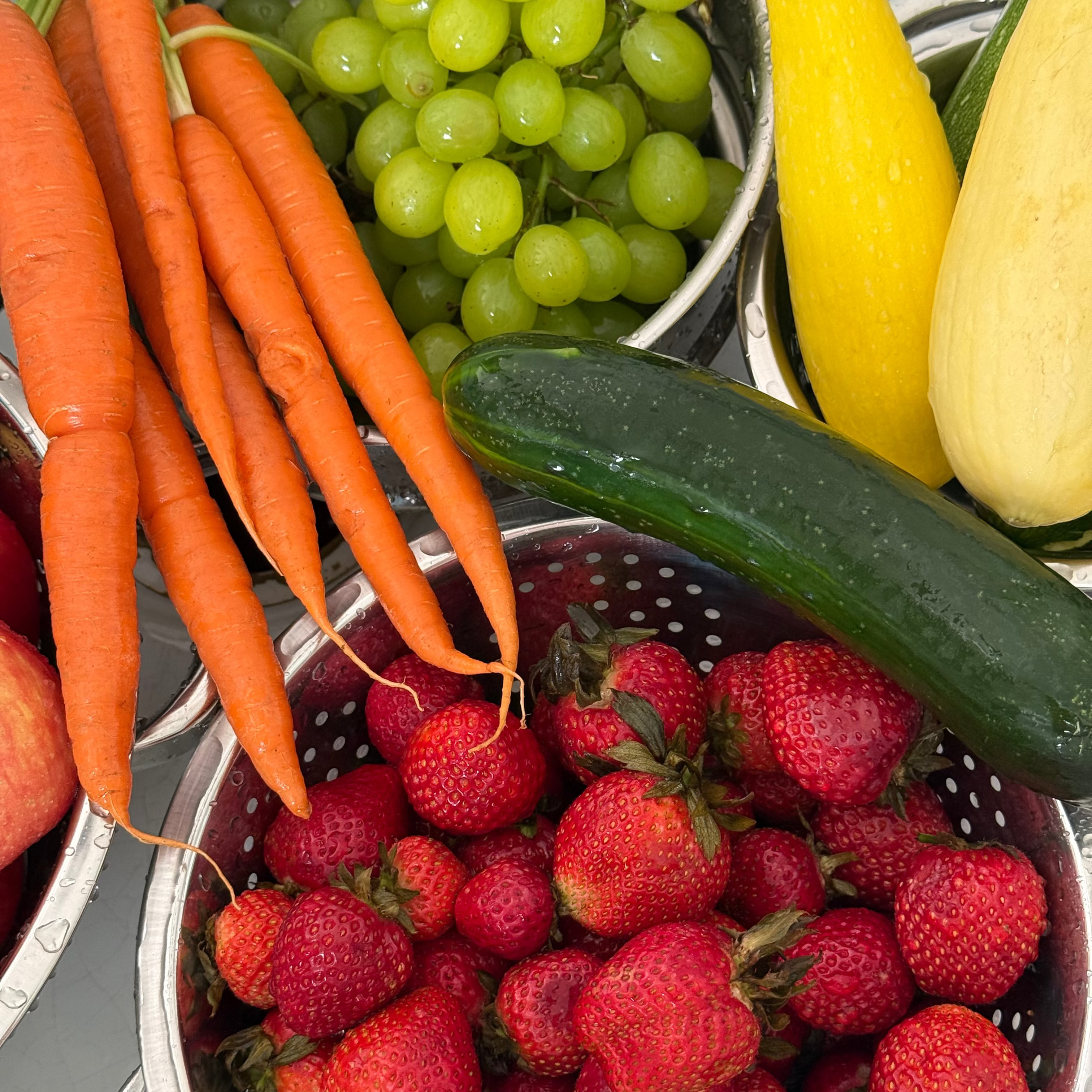 Assorted fruits and vegetables including carrots, grapes, zucchinis, and strawberries on a gray surface.