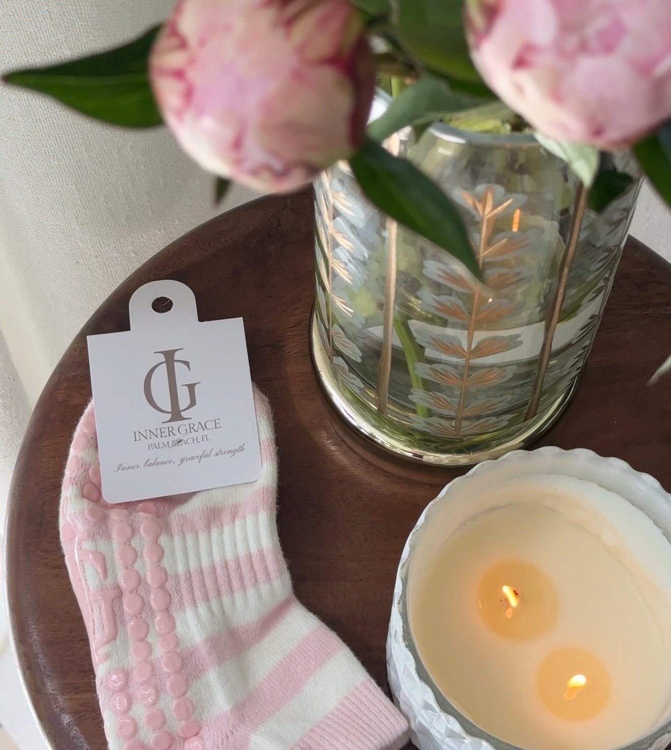Pink socks with a tag, candle, and vase of flowers on a wooden surface