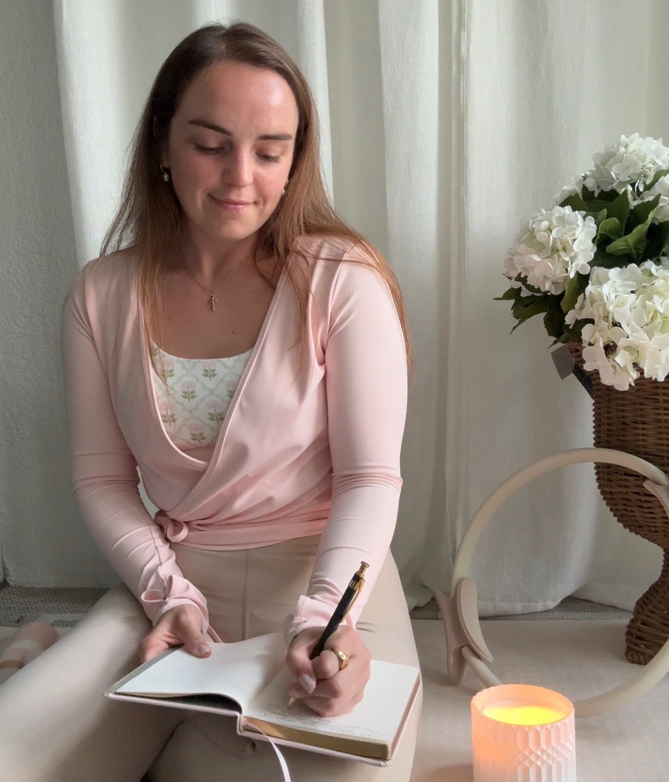 Woman sitting on a chair writing in a notebook with a candle and flowers in the background