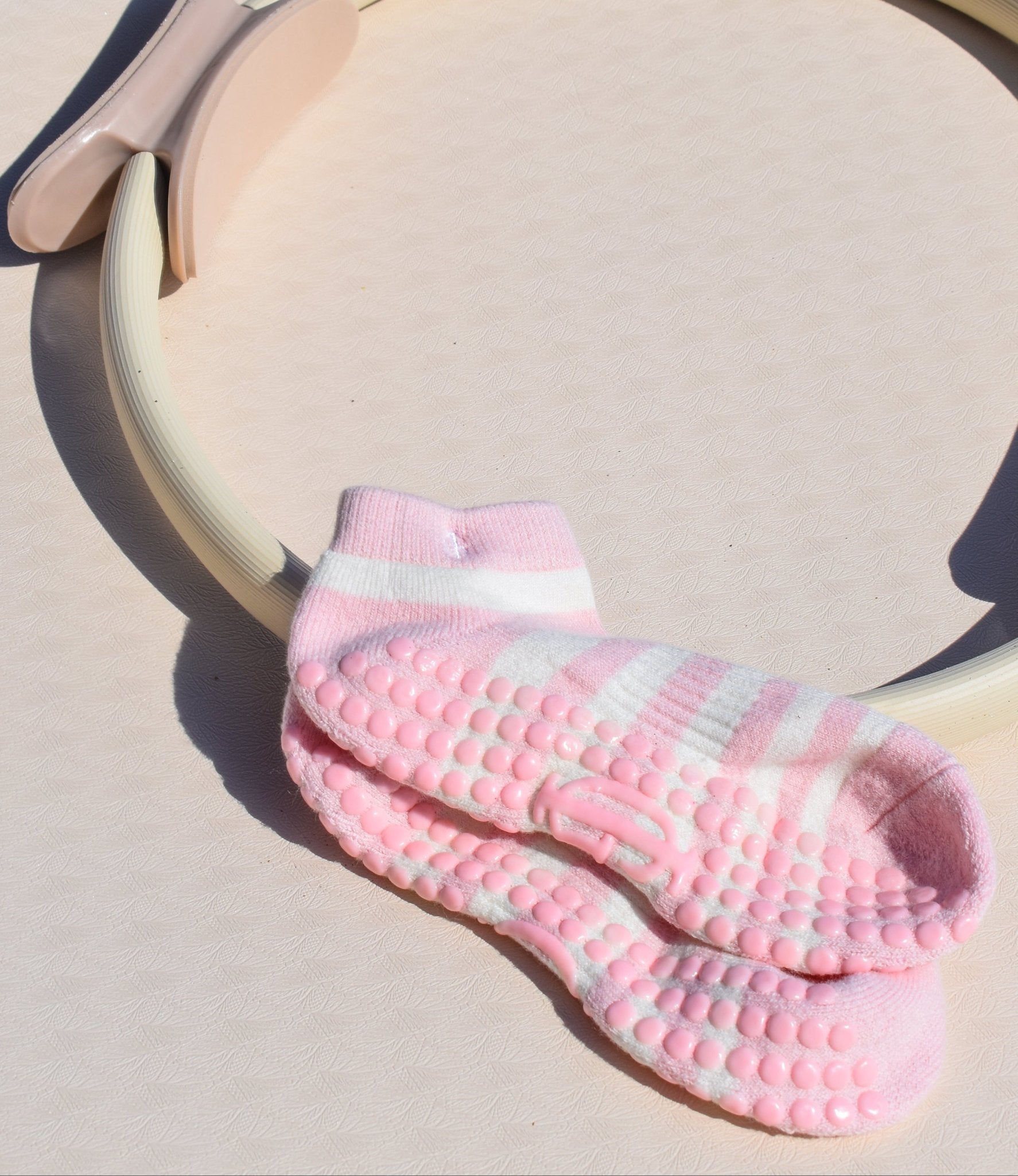 Pink and cream grip pilates socks with textured sole on a beige surface for feminine soft movement